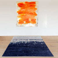 Navy blue rug with an abstract white and gray pattern, complementing an orange and white artwork above.