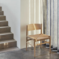 Natural wood chair with a woven seat, featuring neutral tones and subtle textures against a light backdrop.