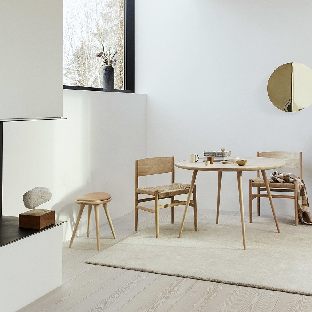 Scandinavian-style dining space featuring natural wood tones, soft beige rug, and minimalist decor in a light, neutral palette.