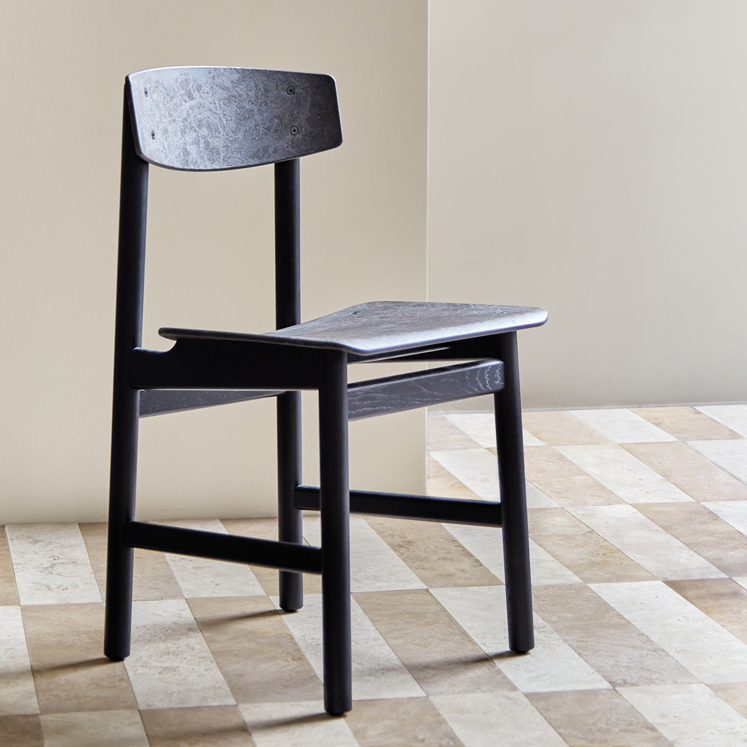 Black wooden chair with a smooth seat and backrest, set against a patterned floor of light and dark beige tiles.