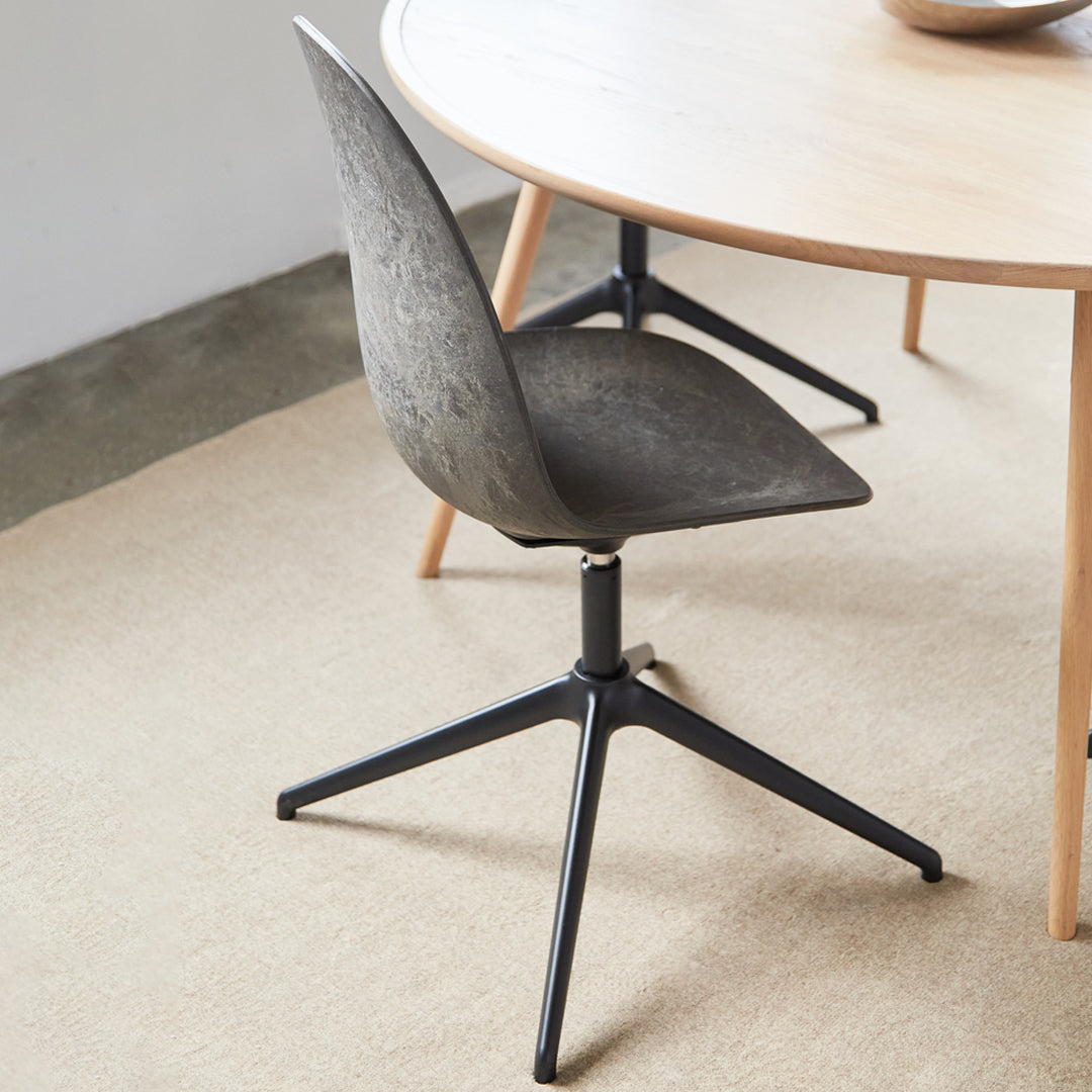 Sleek gray chair with textured pattern and black metallic base, set against a light wood table and neutral rug.