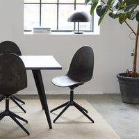 Black modern chair with a smooth curved seat, paired with a minimalistic white table and neutral rug in a stylish interior.