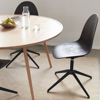 Black swivel chair beside a round light wood table, featuring natural tones and an elegant minimalistic design.