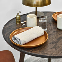 "Brown wooden table with a copper tray, gray napkin, white mugs, glass of water, and brass lamp."