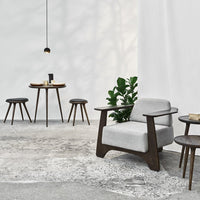 Modern gray upholstered chair with dark wood accents, paired with matching wooden tables and a green potted plant.
