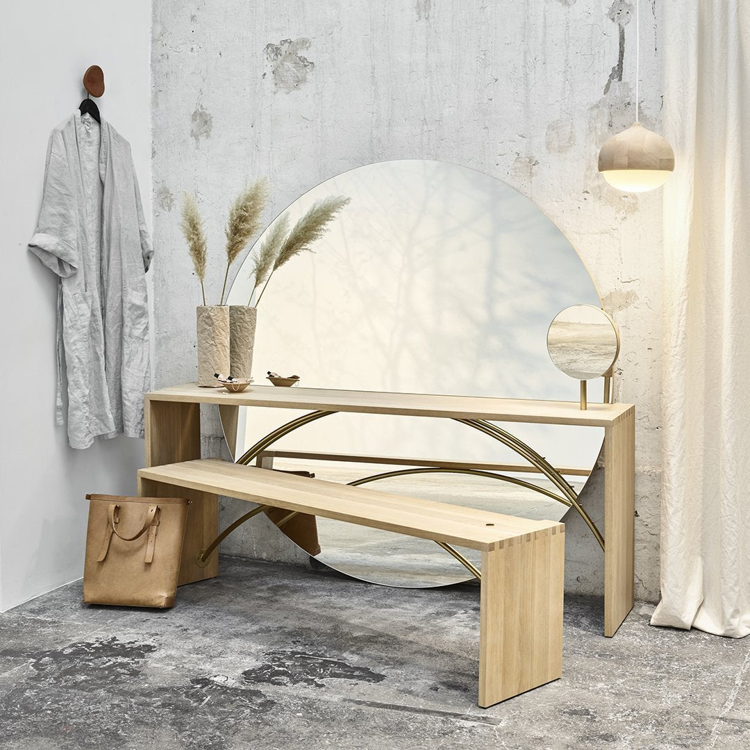 Light wood bench with curved design, neutral tones, and soft shadows against a textured wall. Minimalist decor accents.
