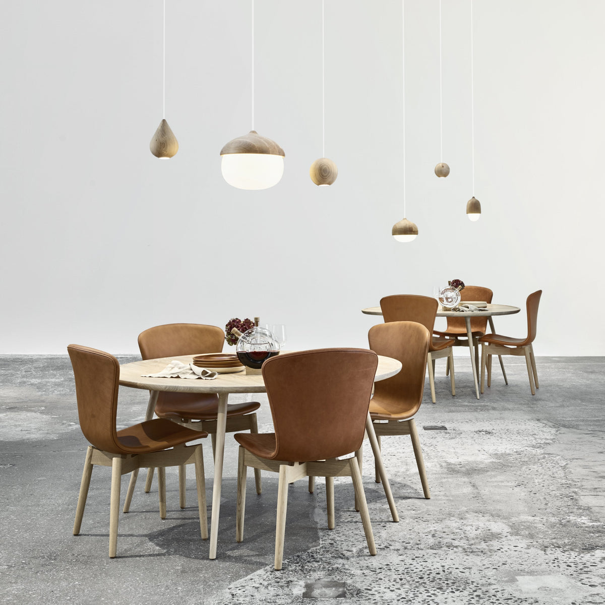 Modern dining table set with beige chairs and light wood accents on a textured gray floor. Pendant lights in natural tones.