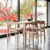 Scandinavian-style dining table with natural wood finish and minimalist design, complemented by vibrant autumn-colored foliage outside.
