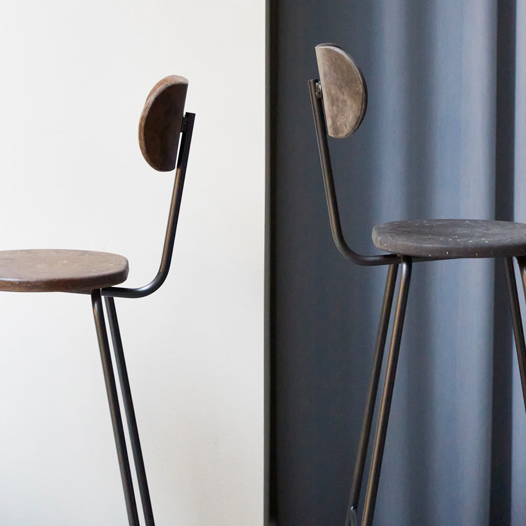 Two minimalist stools featuring dark wood seats and sleek black metal frames, with contrasting round padded backs.