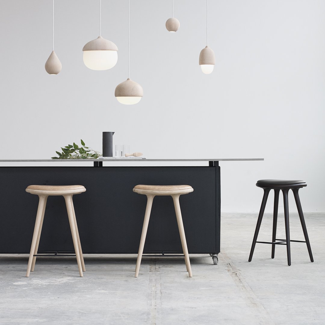 Light wood stools with natural grain, minimalist black island, soft beige pendant lights in a modern kitchen setting.
