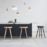Light wood stools with natural grain, minimalist black island, soft beige pendant lights in a modern kitchen setting.