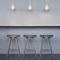 Three sleek, gray bar stools on a modern floor with a soft blue backdrop and minimalist white pendant lights.