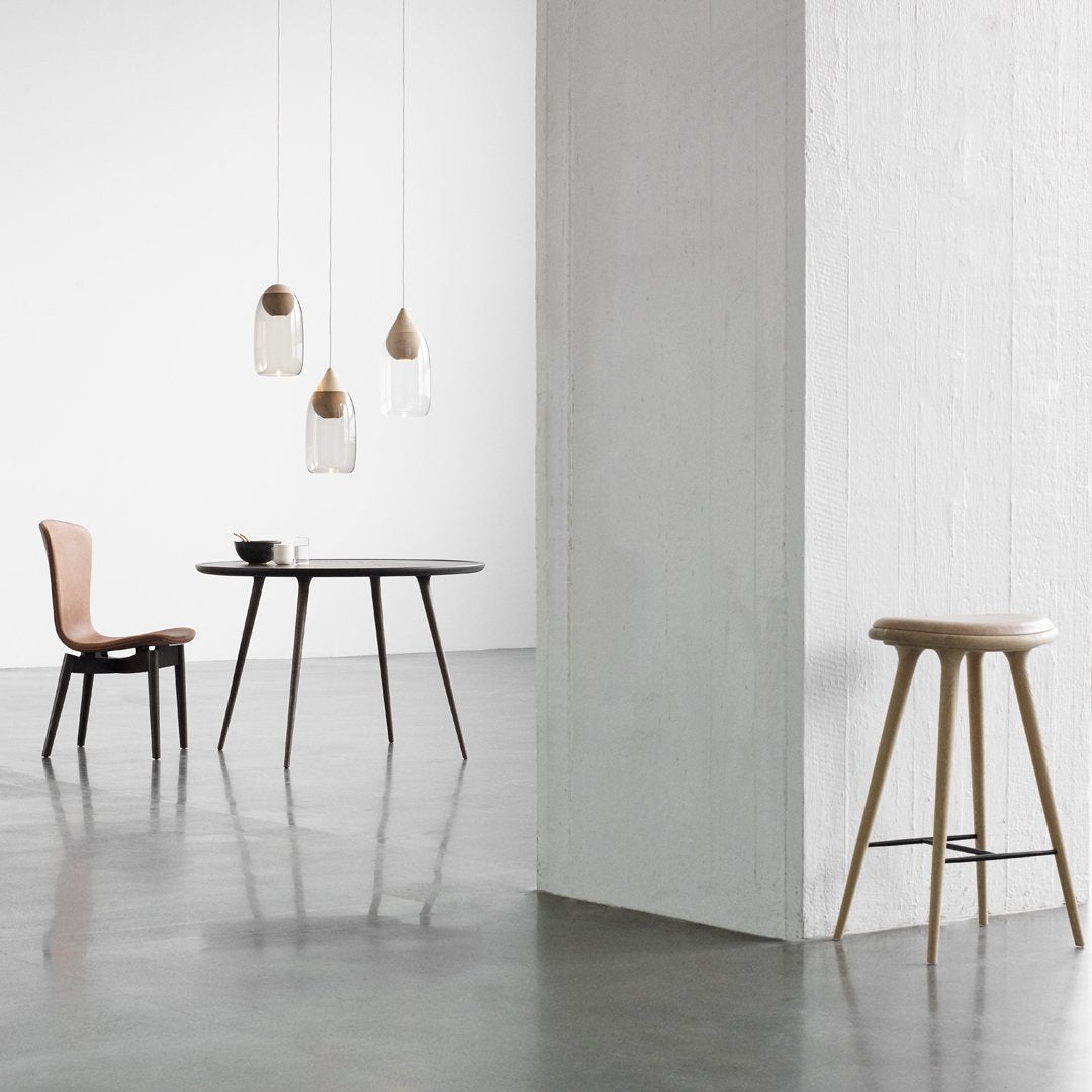Minimalist dining set featuring a black table, warm-toned chairs, and clear glass pendant lights against a light backdrop.