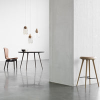 Minimalist dining set featuring a black table, warm-toned chairs, and clear glass pendant lights against a light backdrop.