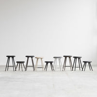 Black, white, and gray stools in various heights and sleek designs, lined up against a minimalist backdrop.