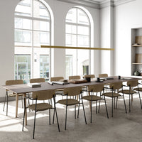 Modern workspace featuring a minimalist wooden table with light beige chairs against a neutral gray floor and bright windows.