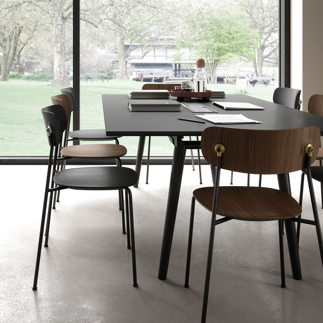 Modern dining table with black surface, complemented by brown wood chairs and sleek metal details, set against a bright backdrop.