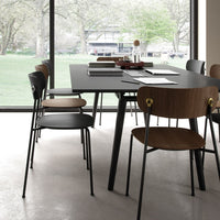 Modern dining table with black surface, complemented by brown wood chairs and sleek metal details, set against a bright backdrop.