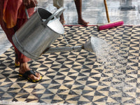 Geometric black and beige patterned floor with a watering can pouring water on it.
