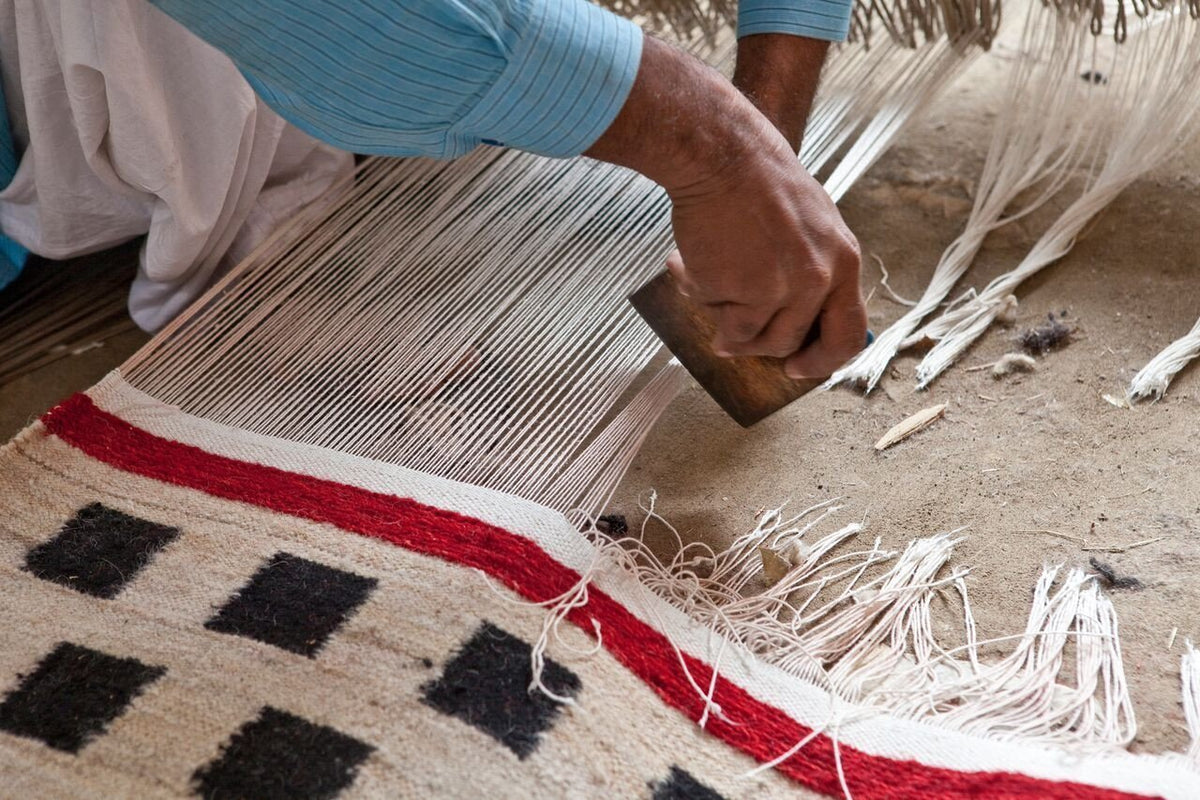 Handwoven rug featuring black and white geometric patterns, with a bold red border and natural fiber tones.