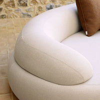 Beige curved sofa arm with textured fabric and a brown accent pillow. Modern design with neutral colors.