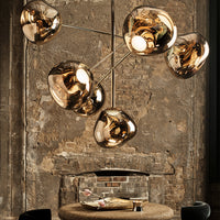 "Modern pendant light with a sleek gold finish and organic, sculptural shapes against a rustic stone background."