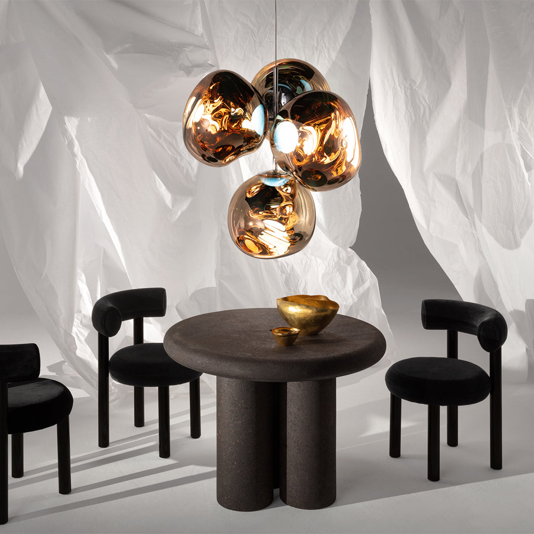 Modern black chairs around a round black table, accented by a gold and metallic light fixture against a soft white backdrop.