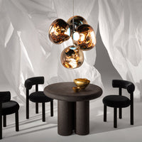 Modern black chairs around a round black table, accented by a gold and metallic light fixture against a soft white backdrop.