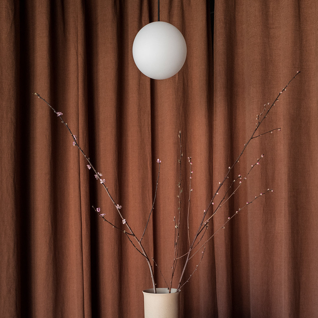 "Warm brown curtains with soft pink flowers on branches, complemented by a round white pendant light."
