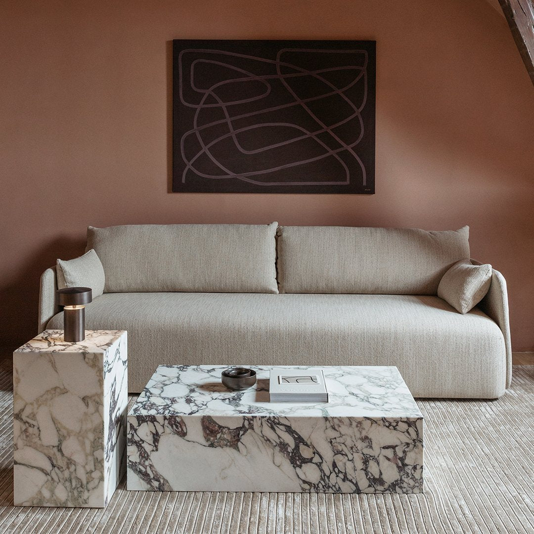 Neutral beige sofa with smooth lines, paired with bold black and white marble coffee tables and a dark abstract wall art.