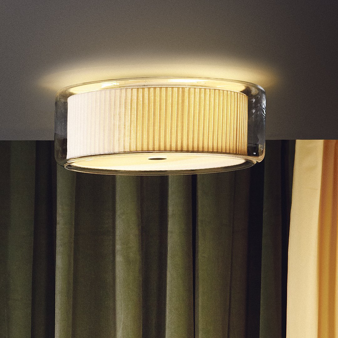 Round ceiling light with a textured cream shade and clear accents, complementing dark green curtains.
