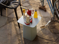 Light blue square table with red, yellow, and white condiment bottles on top, set against a textured stone surface.