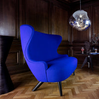 Vibrant blue lounge chair with a smooth texture, set against a dark wood background and geometric patterned flooring.