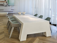 Modern white dining table with sleek lines, paired with muted green chairs on a herringbone wood floor.