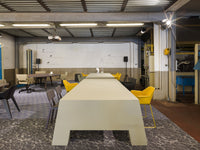 Modern workspace with a light gray table, yellow chairs, and neutral wall colors, featuring a textured floor pattern.