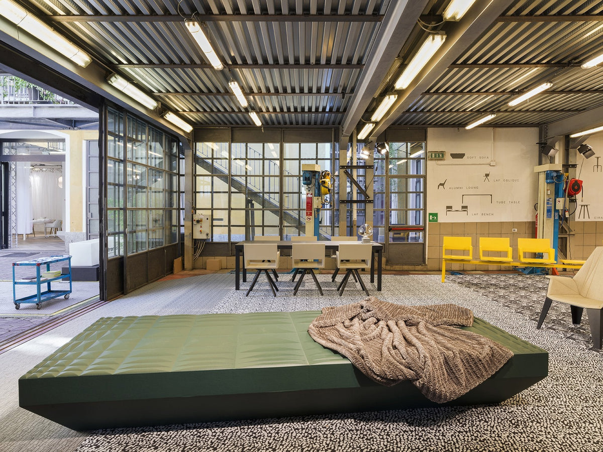 Green geometric sofa with a textured gray blanket, set against a modern industrial background with patterned flooring.