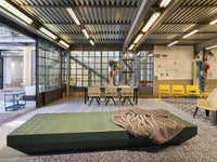 Green geometric sofa with a textured gray blanket, set against a modern industrial background with patterned flooring.