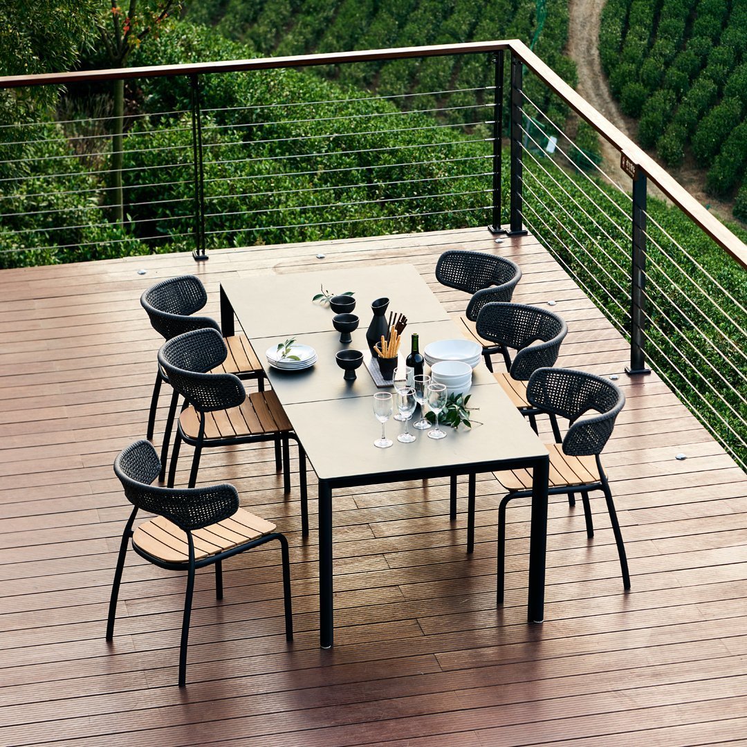 "Modern black and wood dining set on a wooden deck, surrounded by lush greenery."