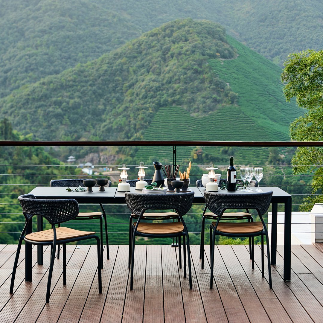 "Elegant black dining table with natural wood accents, surrounded by lush green hills and a scenic backdrop."