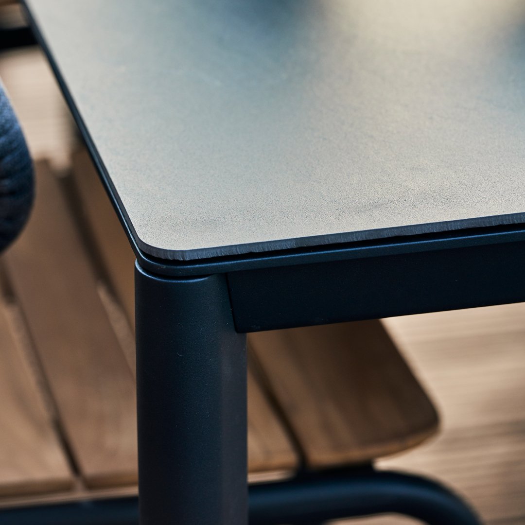 Black tabletop with smooth surface and sleek edges, paired with a wooden chair showing a natural wood grain pattern.