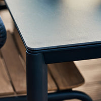 Black tabletop with smooth surface and sleek edges, paired with a wooden chair showing a natural wood grain pattern.