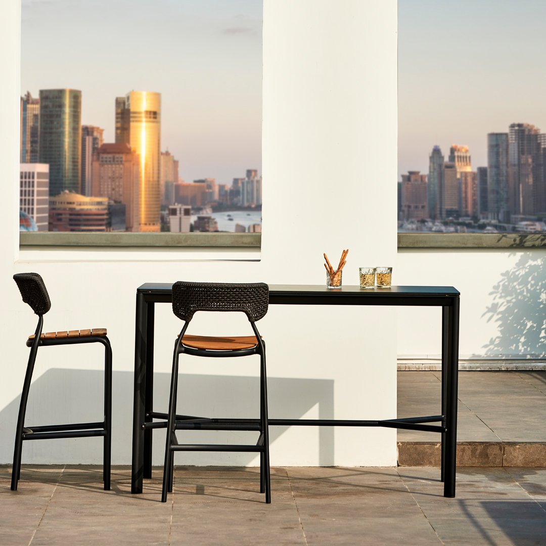 Black metal bar table with wooden accents, paired with matching black and wood bar stools against a skyline backdrop.
