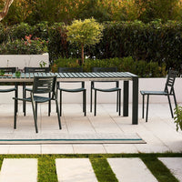 "Outdoor dining set featuring a sleek black table and matching green chairs, complemented by a striped runner on the patio."