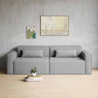 Gray patterned sofa with two matching cushions, set against a minimalist concrete wall and light wooden floor.