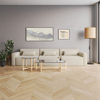 Modern beige sofa with light wood furniture against a soft gray wall and herringbone wood flooring. Minimalist decor.
