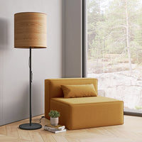 Modern yellow upholstered chair with a brown wooden floor lamp, set against a natural landscape backdrop.