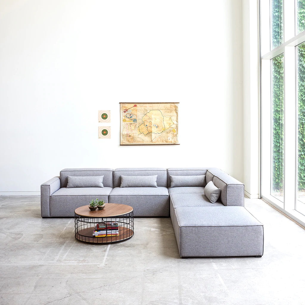 Gray L-shaped sofa with minimalist design, featuring subtle texture and matching pillows in a bright, airy room.