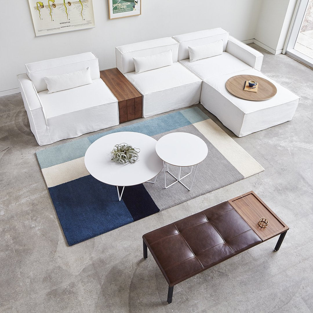 Modern white sectional sofa with wood accents, accompanied by a geometric rug in shades of blue and cream. Stylish decor.
