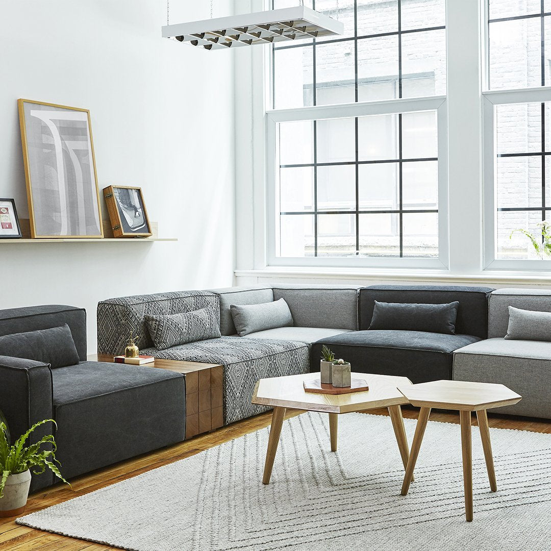 Modern sectional sofa in gray tones with a textured pattern, complemented by a light area rug and wooden accents.