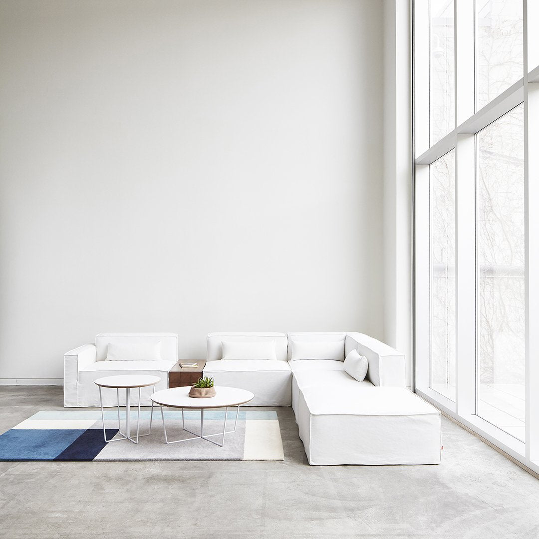 White sectional sofa with a light grey floor and patterned blue and cream rug, enhancing a modern minimalist aesthetic.